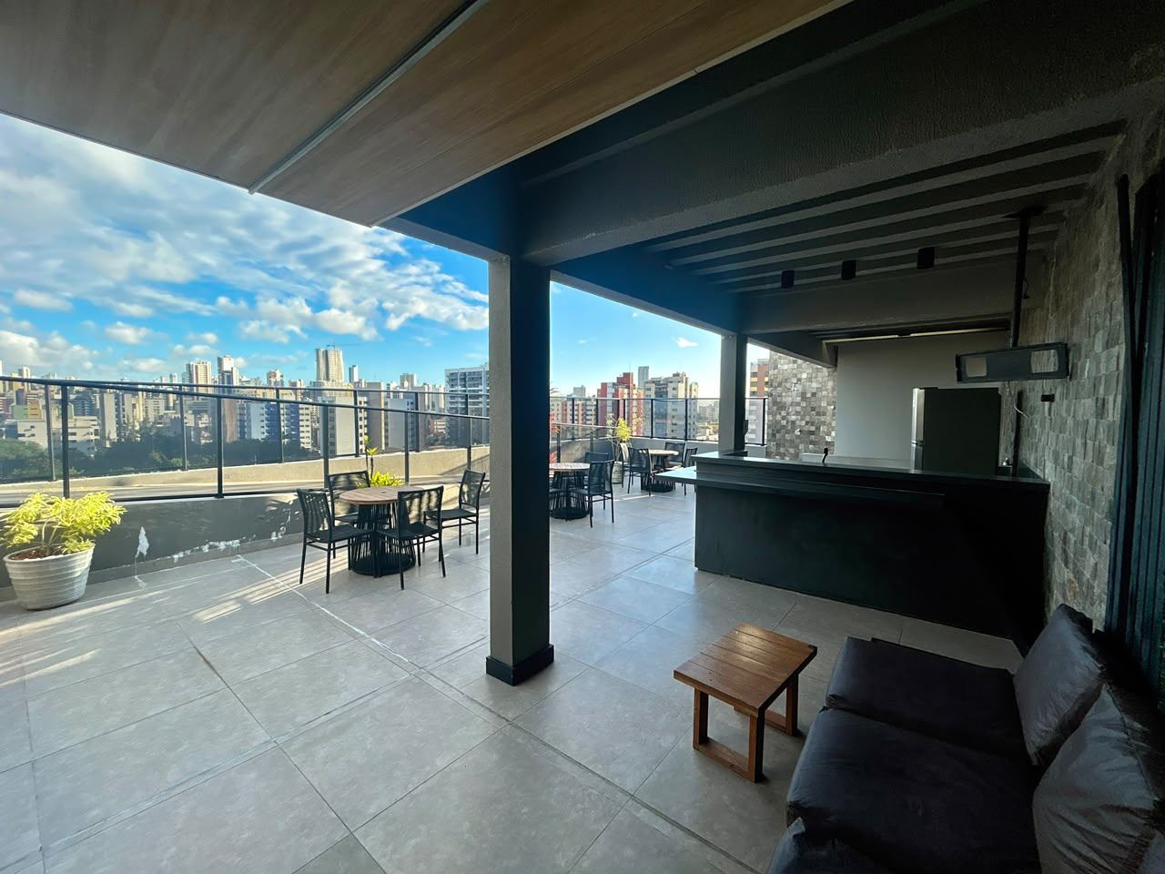 Espaço coberto do rooftop com churrasqueira e mesas, área comum
